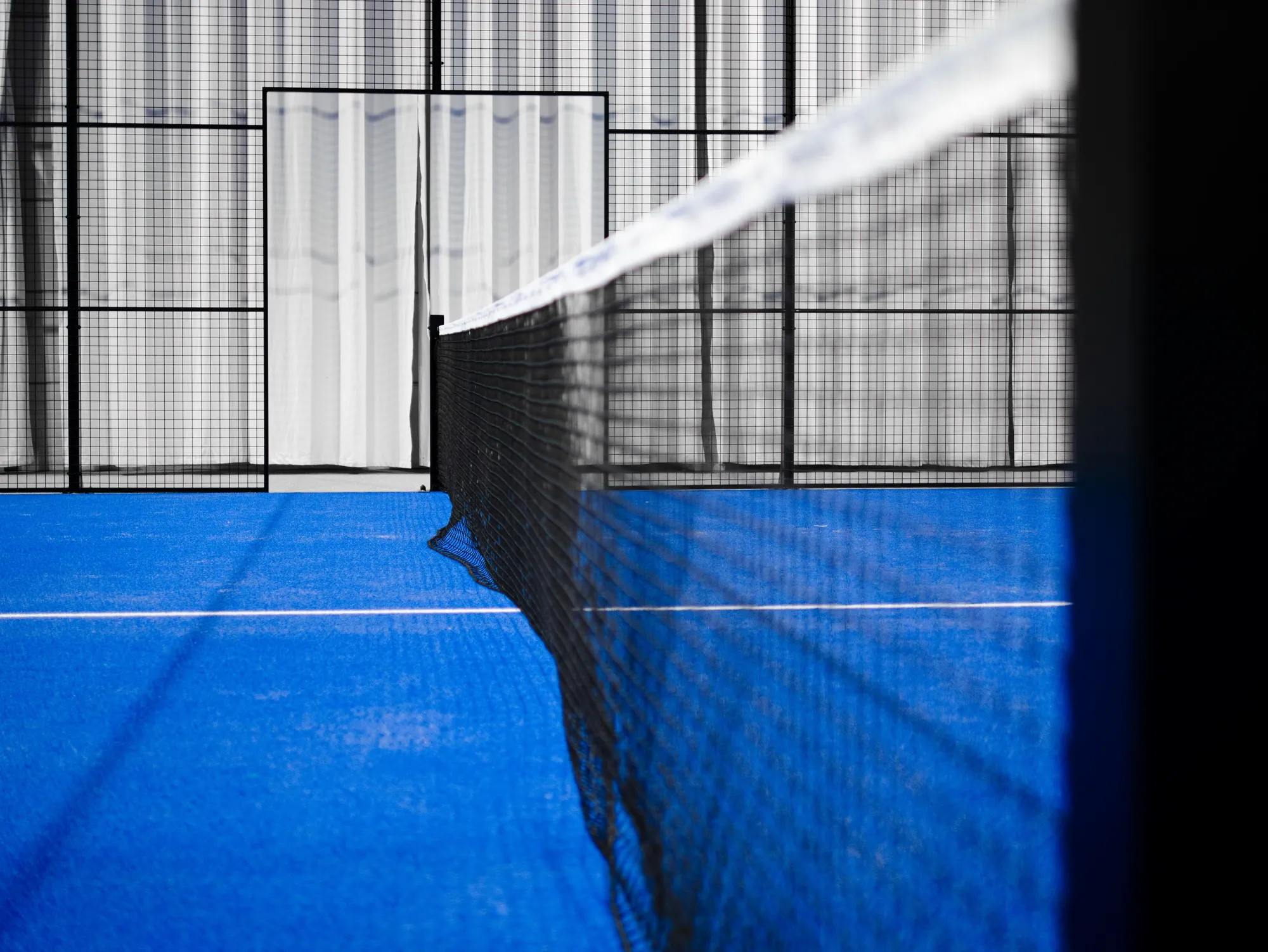 Le filet et la surface bleue d’un terrain de padel couvert.