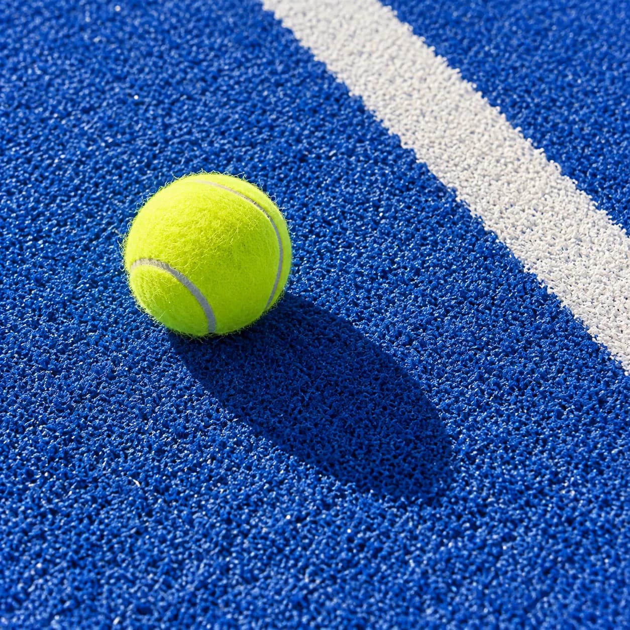 Une balle de padel jaune sur la surface bleue du terrain.