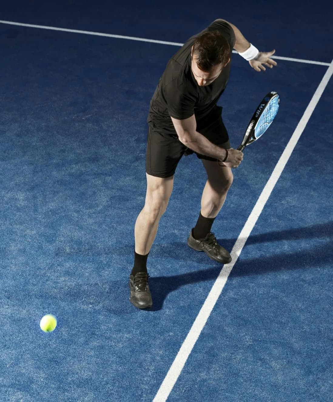 Un joueur prépare sa frappe sur un terrain de padel bleu.