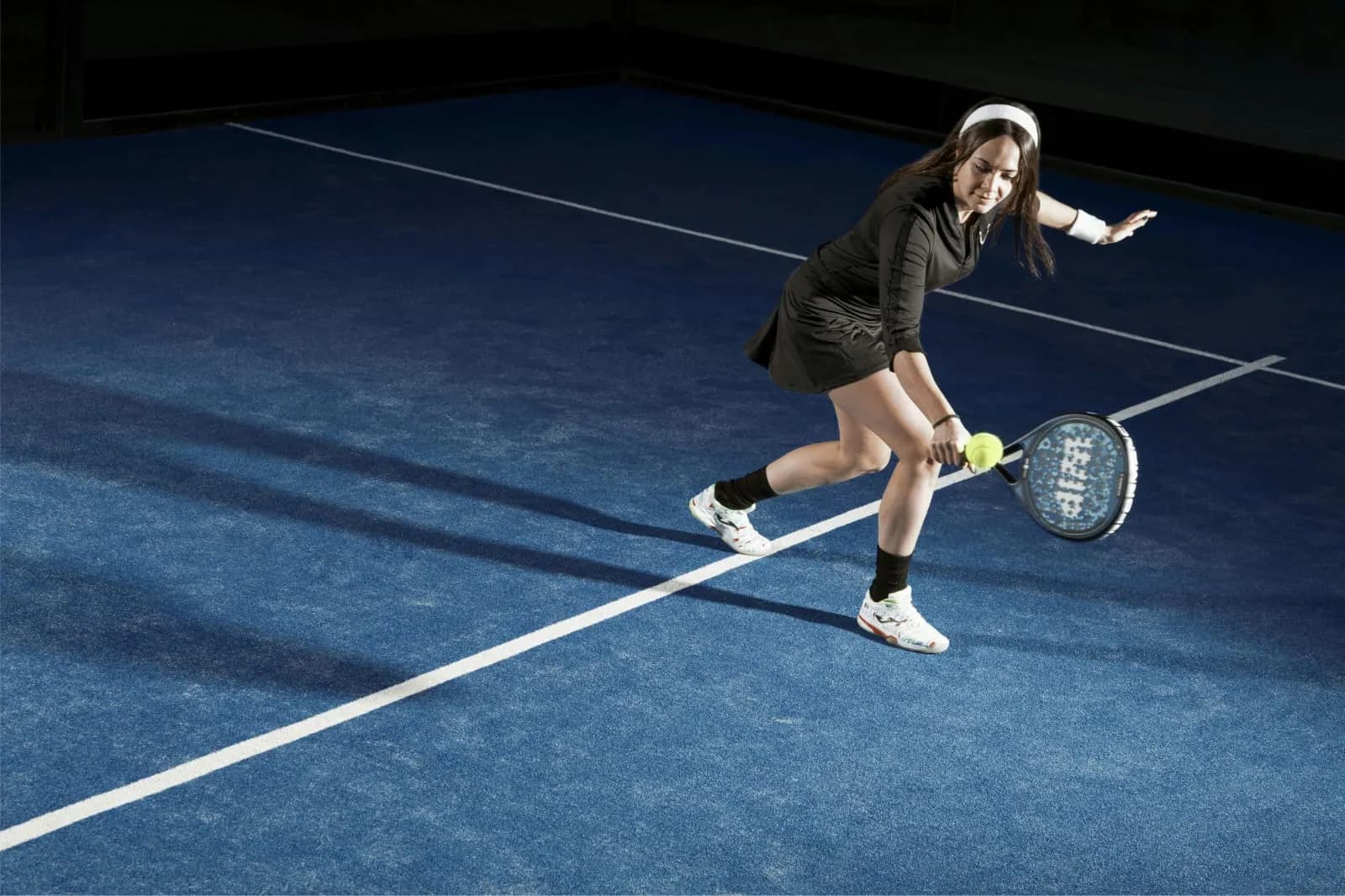 Une joueuse de padel frappe la balle sur un terrain bleu.